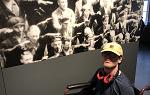 Student in wheelchair with glasses and yellow baseball cap poses for picture in front of a large black and white image in the German Resistance Memorial Center.  