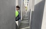 一个穿着绿色t恤的学生站在迷宫一样的建筑里，在走下一条过道之前，他回头看着镜头.