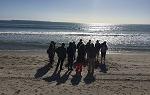 2018年夏季新西兰留学之旅的学生们站在海滩上，太阳在海洋地平线上落下. 